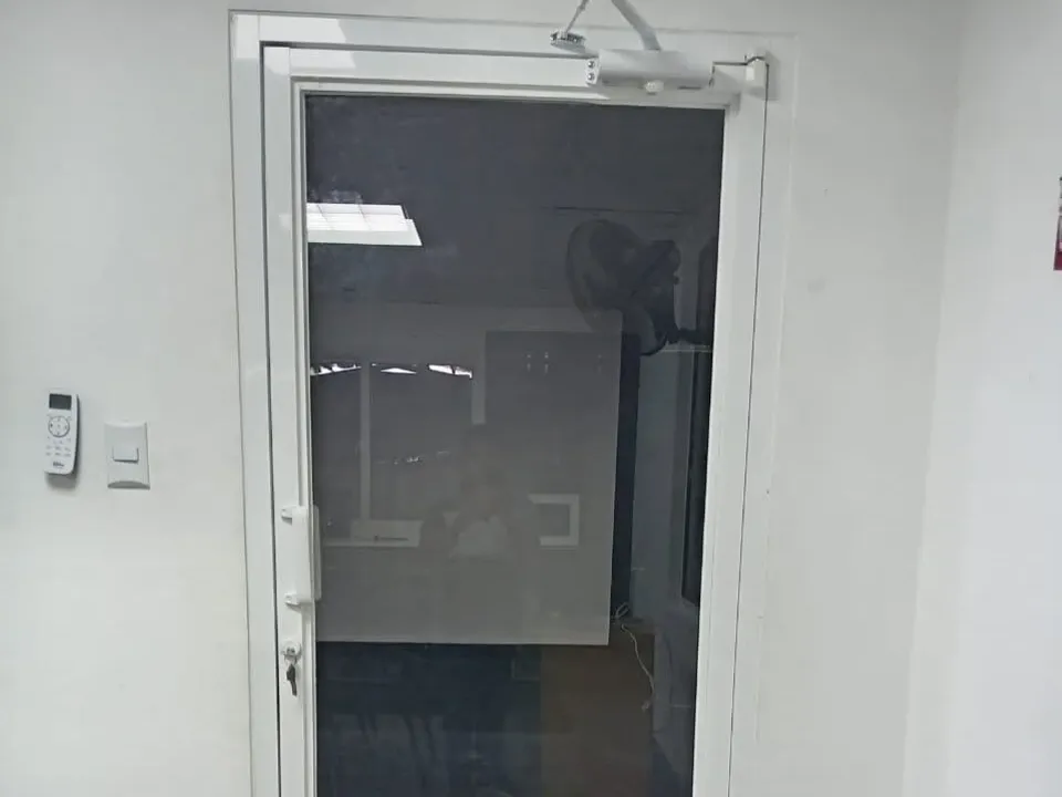 Puerta de vidrio con marco de aluminio blanco y cierrapuertas instalada en una oficina