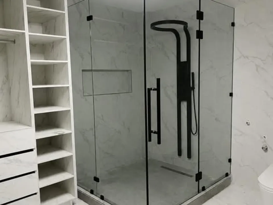 Cabina de baño en vidrio templado con herrajes negros instalada en un baño de mármol